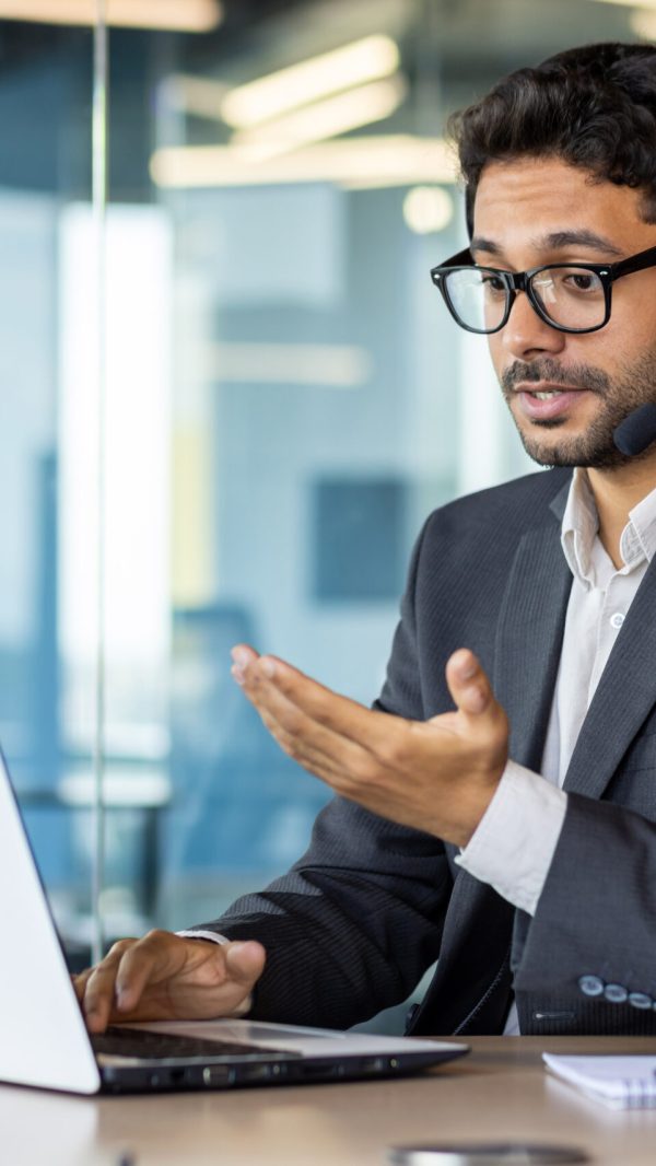 Serious concentrated and thinking businessman with headset phone for video call looking at web camera on laptop, man in business suit boss discreetly talking remotely with colleagues and partners.